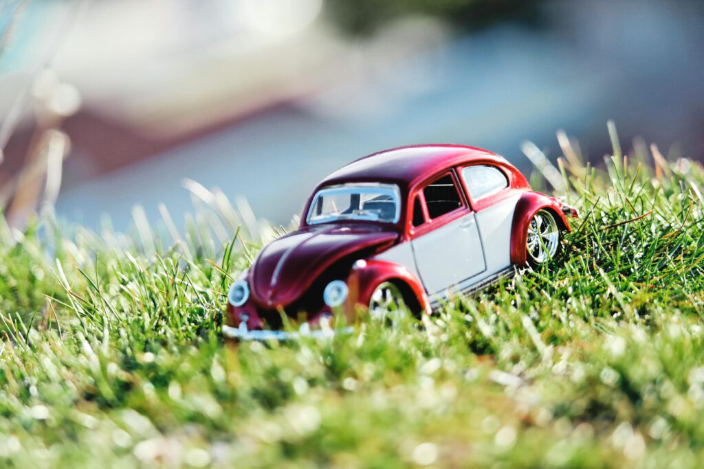 A red and white toy Volkswagen Beetle car on a sunny grass field during summer.