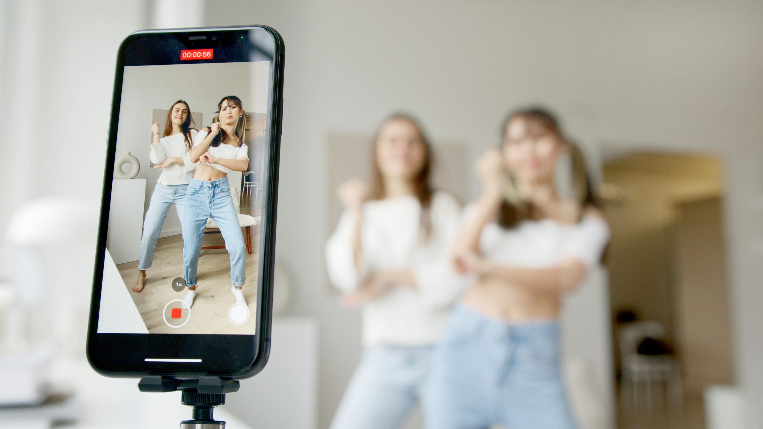 Two women dance in front of a smartphone camera, recording content indoors.